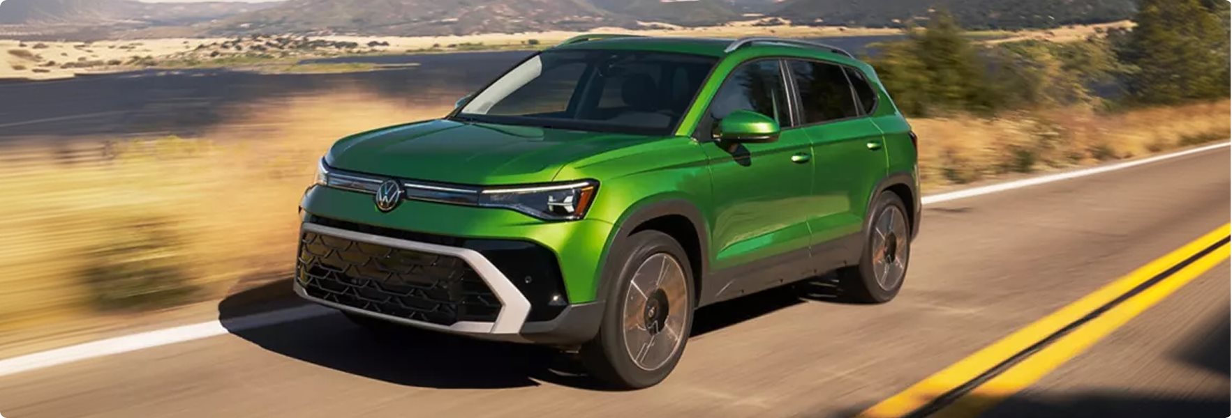 Green 2027 Volkswagen Taos driving along a highway past sunlit hills
