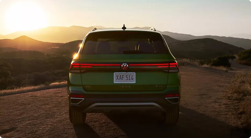 Rear of a green 2027 Volkswagen Taos with its LED taillight bar and illuminated VW logo lit at sunset