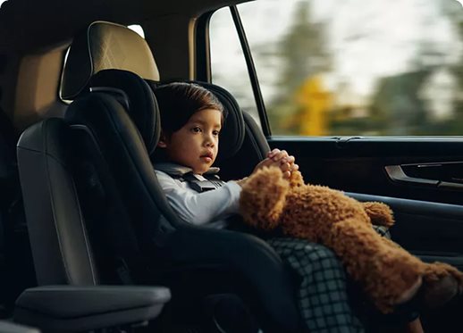 Young child in a car seat holding a teddy bear in the back seat of a Volkswagen