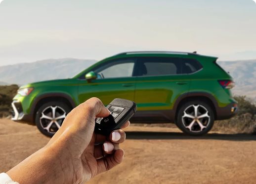Hand holding a Volkswagen key fob in front of a green Taos