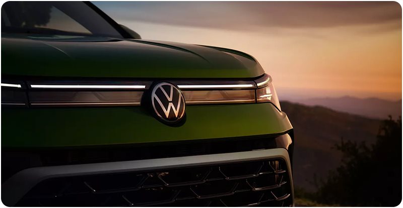 Illuminated light bar and VW logo on the grille of a green Taos at sunset