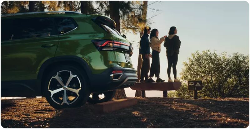 Green Volkswagen Taos parked beside three friends standing on a bench at a scenic overlook