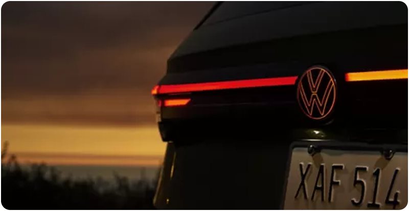 Illuminated VW logo and taillight bar on the rear of a Taos at sunset