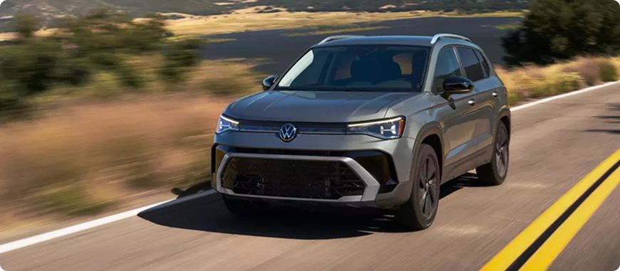 Grey 2027 Volkswagen Taos Sport driving on a highway with yellow road markings