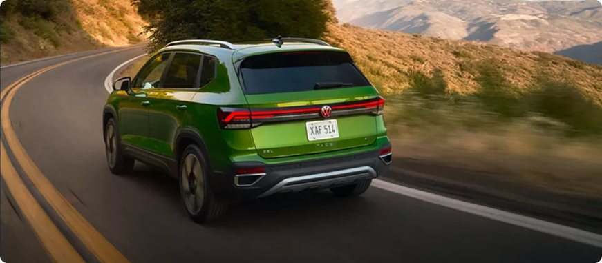 Green Volkswagen Taos taking a curve on a winding hillside road