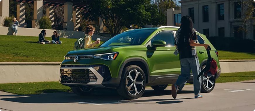 Woman walking up to a green Volkswagen Taos parked on a campus street