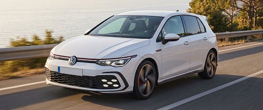 White Volkswagen hatchback driving along a coastal highway