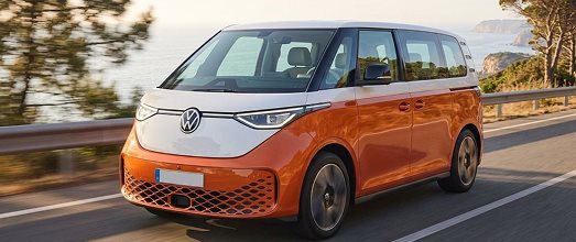 Orange and white Volkswagen electric van driving along a coastal highway