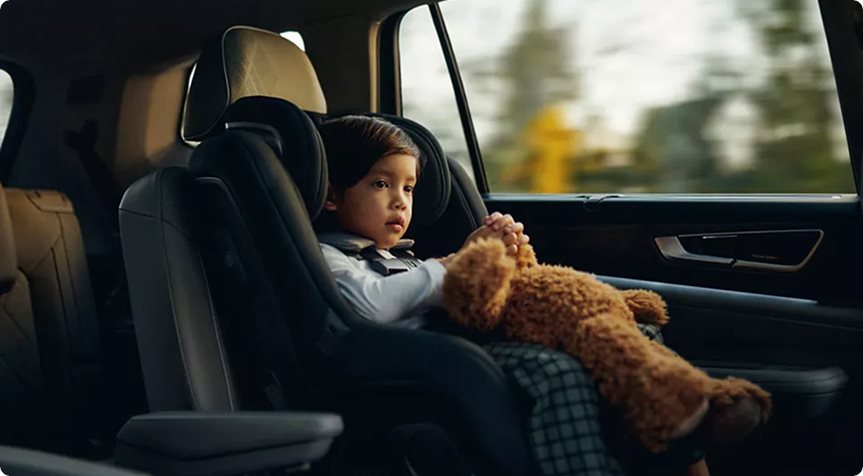 Young child in a car seat holding a teddy bear in the back seat of a Volkswagen