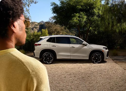 Man in a yellow shirt looking at a white Volkswagen SUV parked outdoors