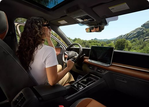 Woman driving a Volkswagen with a panoramic sunroof through green hills