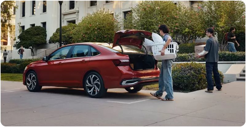 Two friends loading laundry baskets into the open trunk of a red Volkswagen Jetta