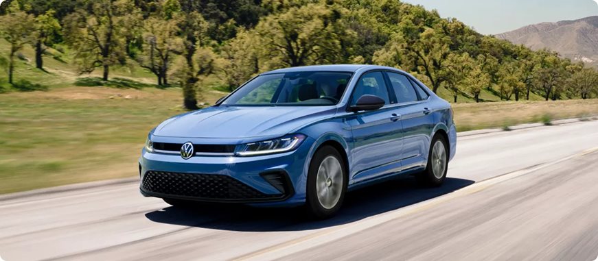 Blue Volkswagen Jetta Sport driving along a road lined with trees