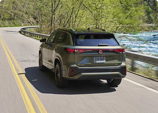 Green 2026 Volkswagen Tiguan SEL R-Line Turbo driving along a riverside road, seen from the rear