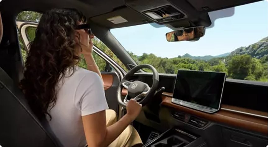 Woman driving a Volkswagen Tiguan past green hills with the touchscreen beside her