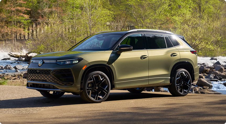 Green 2026 Volkswagen Tiguan parked by a river with rocks and trees behind it