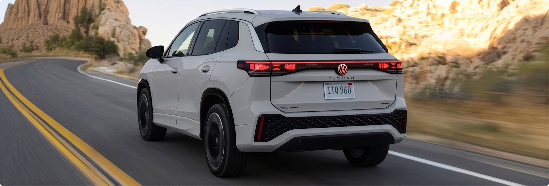 White 2026 Volkswagen Tiguan driving on a desert road, seen from the rear with its light bar lit