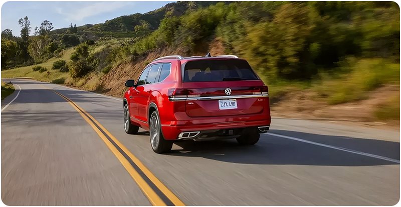 Red Volkswagen Atlas driving along a hillside road, seen from the rear