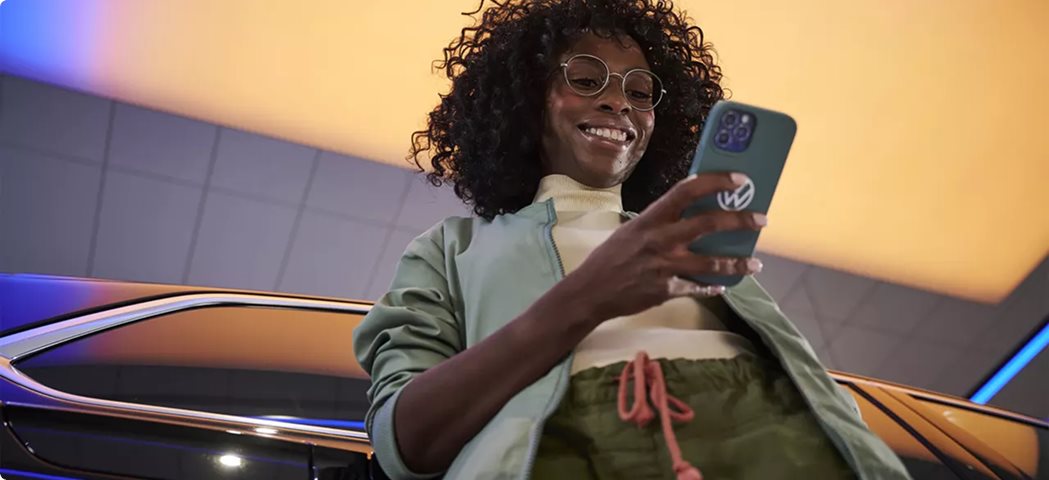 Smiling woman using the myVW app on her phone beside a Volkswagen