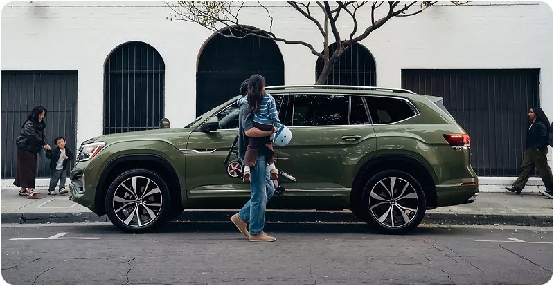 Family walking beside a green Volkswagen Atlas parked on a city street