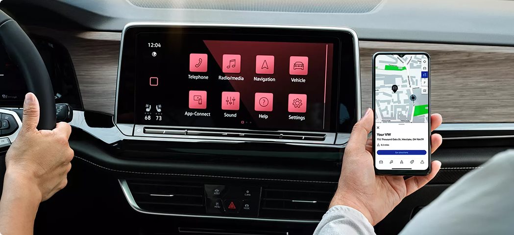 Driver holding a phone with a map beside the Volkswagen Atlas touchscreen