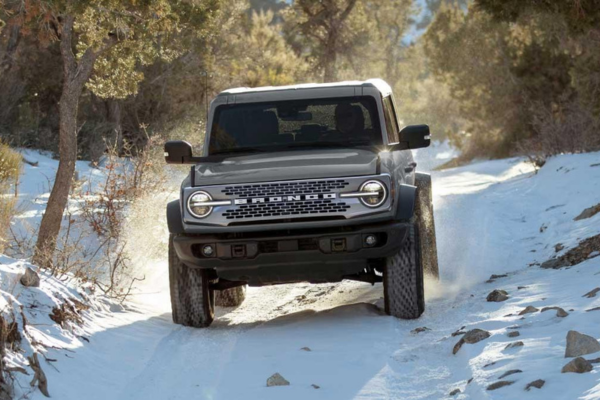 Ford Bronco driving through snow on a rugged, tree-lined trail.