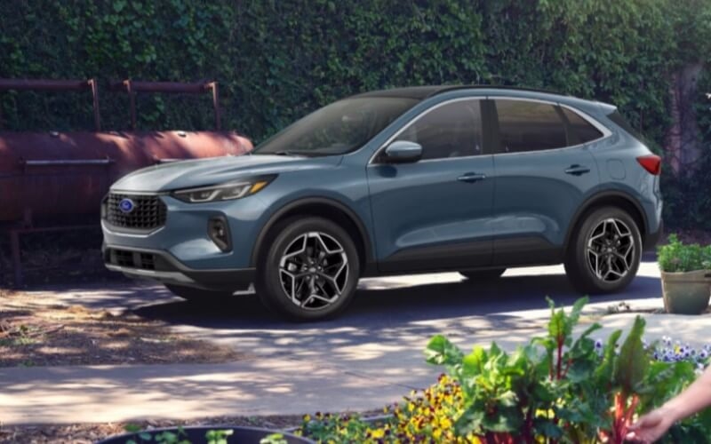 A blue 2026 Ford Escape sits parked next to an outside garden.