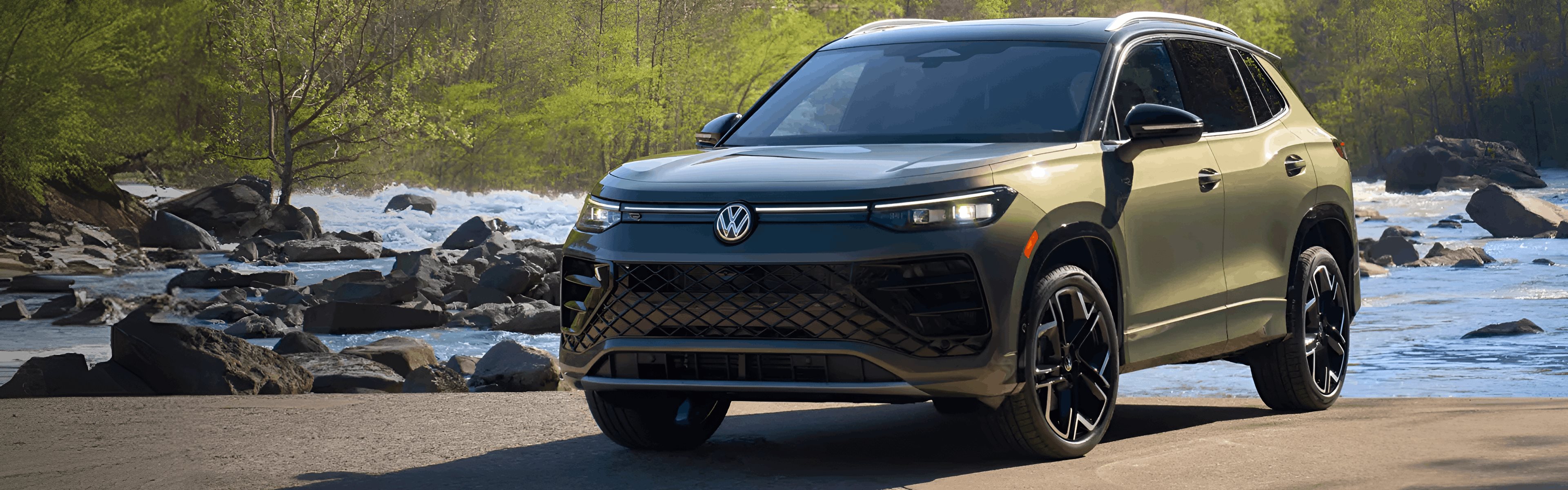 Green 2026 Volkswagen Tiguan parked on a riverbank beside rocky rapids
