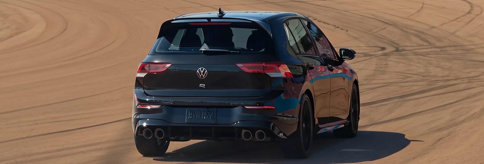 Black 2026 Volkswagen Golf R drifting on a dirt track, seen from behind