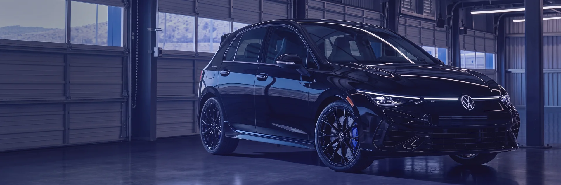 Black 2026 Volkswagen Golf R Hatchback parked in a dim garage with its headlights on