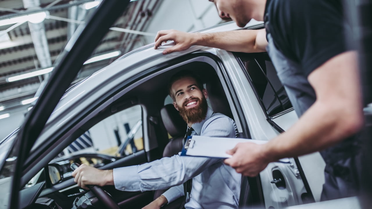 Service technician speaking with a smiling driver seated inside a vehicle.