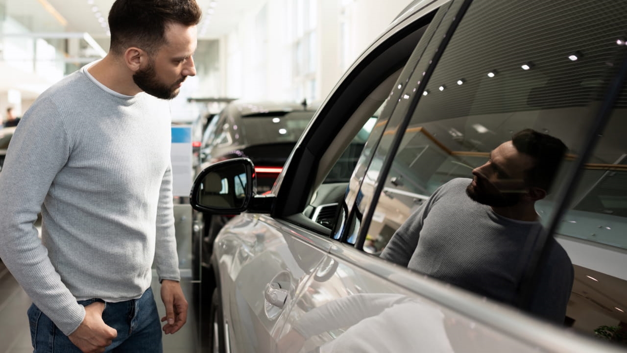 Man inspecting the side of a vehicle inside a car dealership showroom.