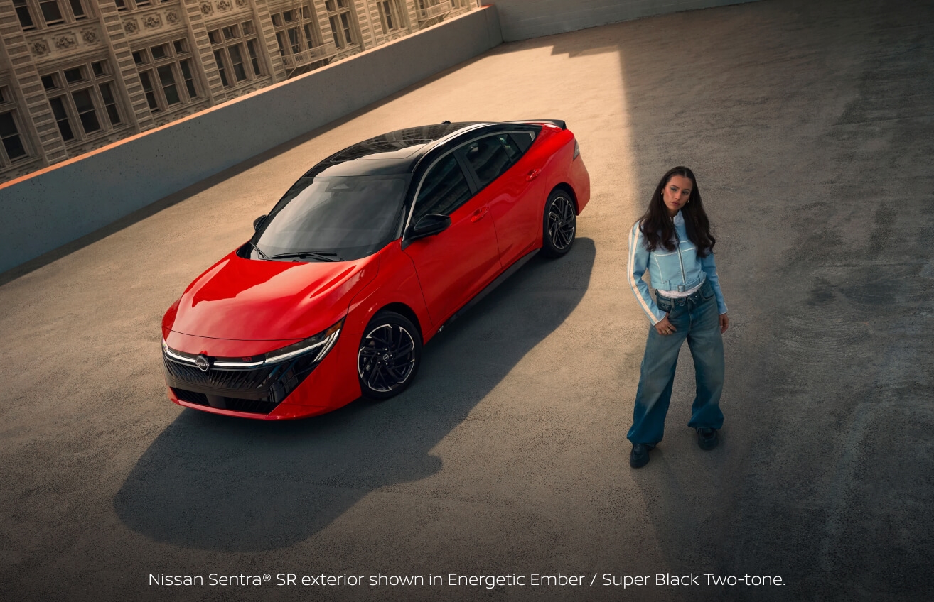 High-angle view of a 2027 Nissan Sentra SR in Energetic Ember and Super Black beside a woman in a blue jacket.