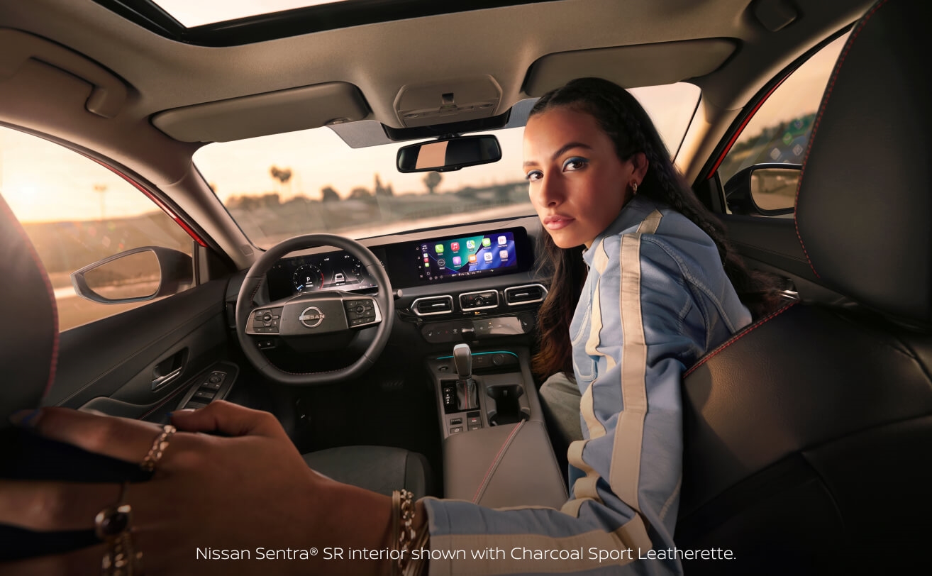Interior view from the back seat of a woman in the passenger seat of a 2027 Nissan Sentra SR with Charcoal Sport Leatherette interior.