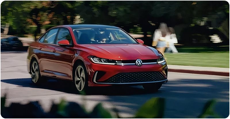 Red Volkswagen Jetta driving along a tree-lined street