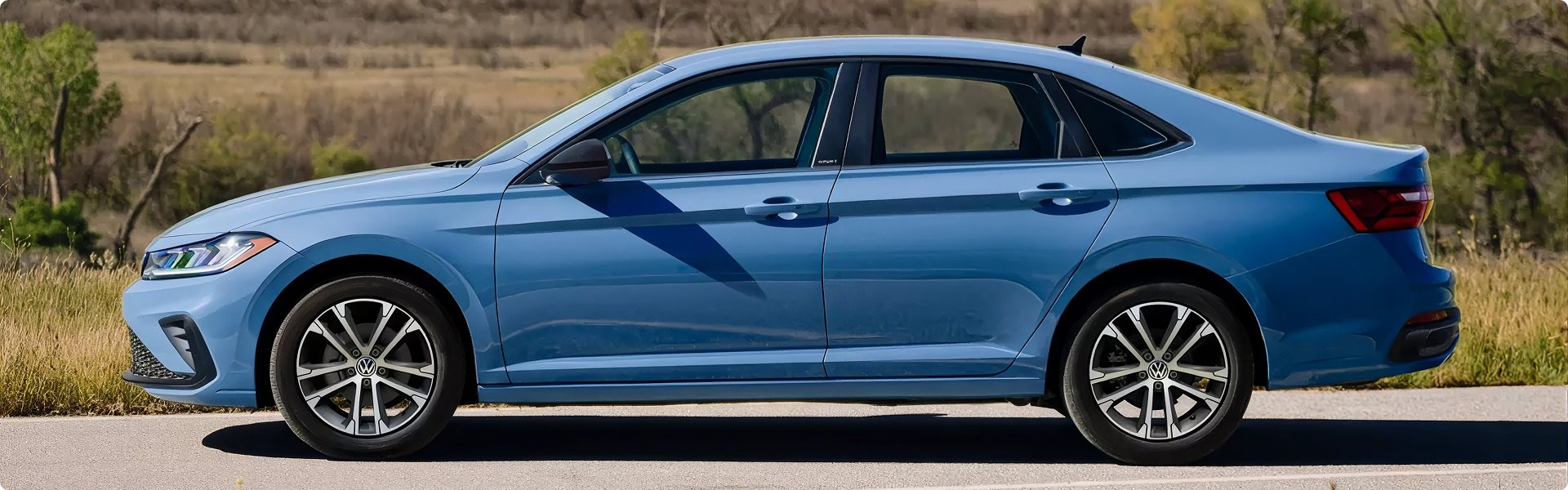 Side view of a blue 2027 Volkswagen Jetta parked beside a field