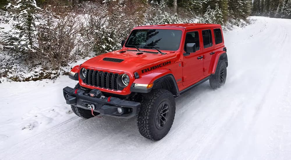 Red 2026 Jeep Wrangler driving down a snowy road.