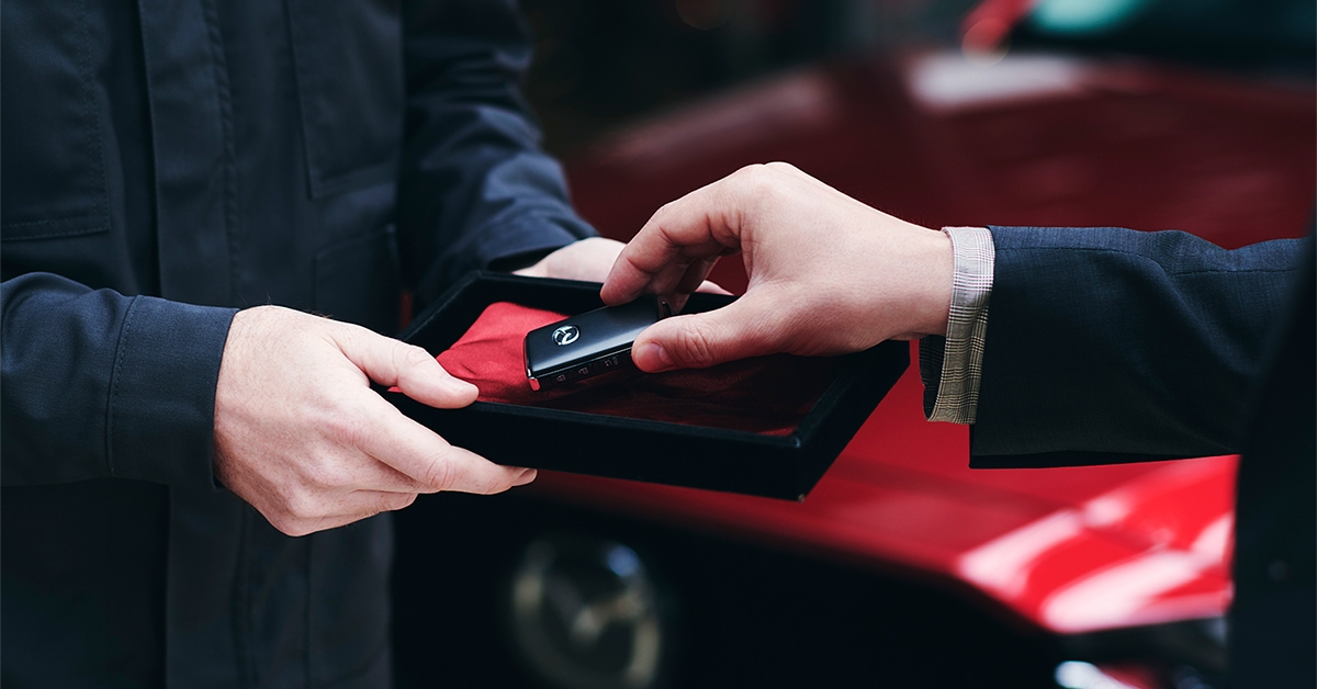Tags: Hands of dealer handing customer key in front of Red Mazda vehicle