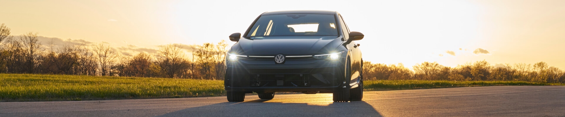 Front view of a dark grey Volkswagen Golf GTI on a rural road at sunset.