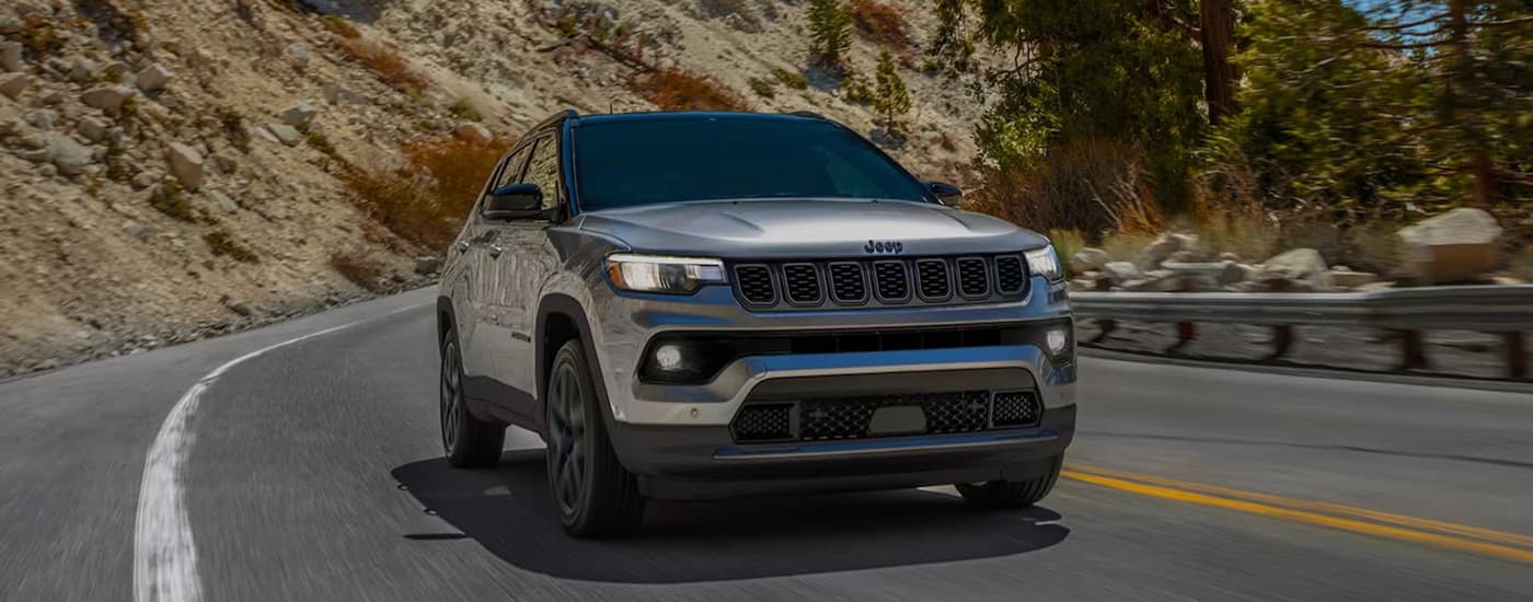 A silver 2026 Jeep Compass driving down a road