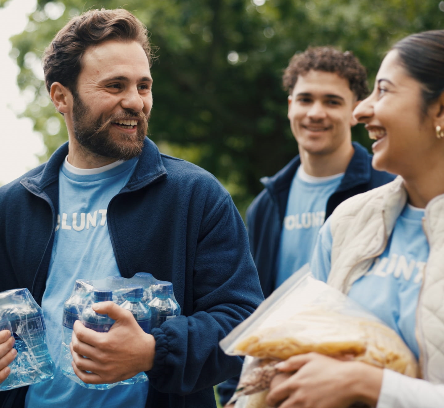 Volunteers carrying bottled water and food donations outdoors.