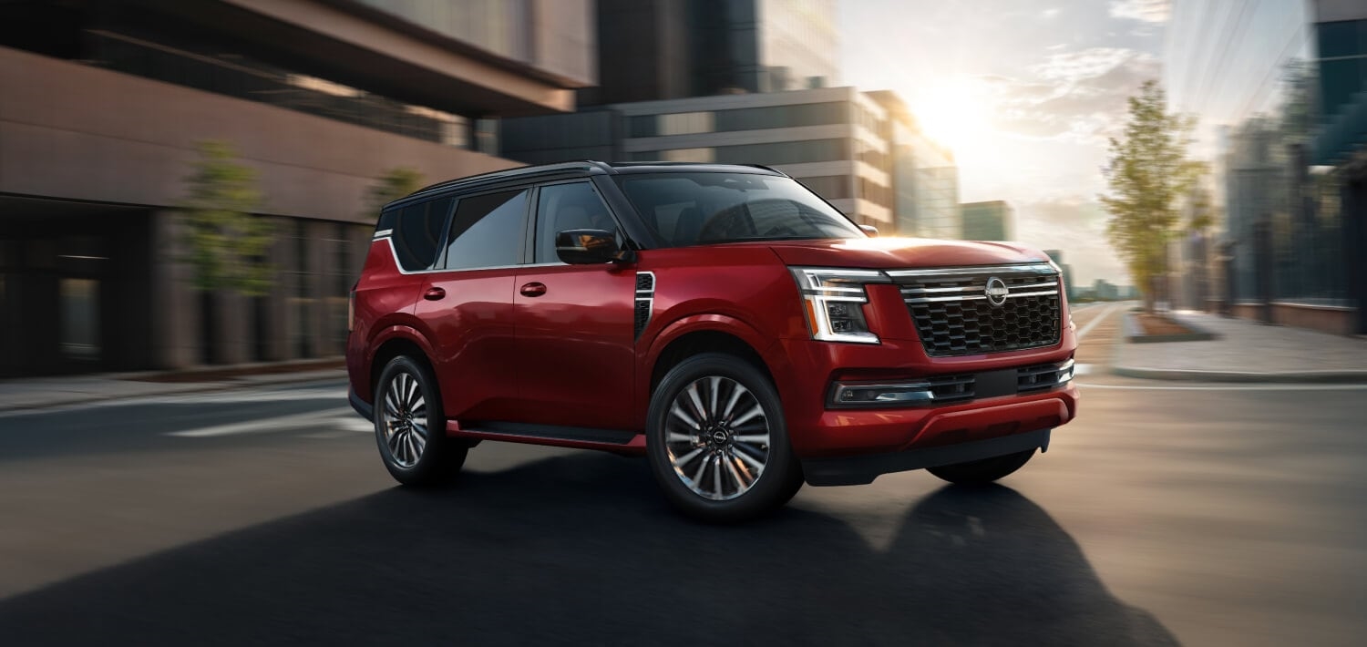 Red 2026 Nissan Armada with a contrasting black roof driving through a city, viewed from the front three-quarter angle.