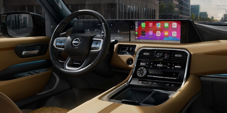 2026 Nissan Armada cockpit with brown trim, steering wheel, wide digital displays and center console.