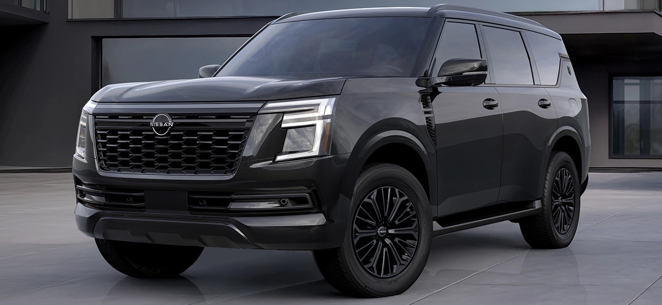 2027 Nissan Armada Dark Armor parked outside a modern building, viewed from the front three-quarter angle.