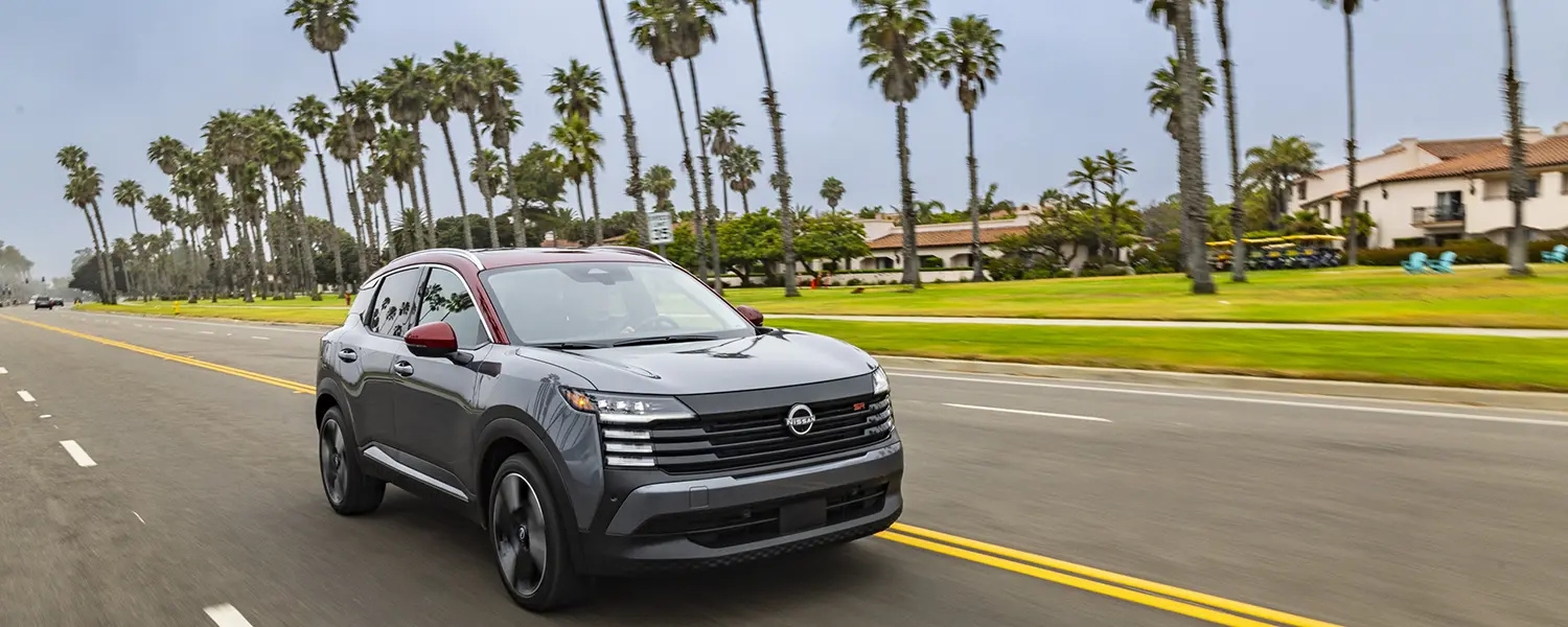 2026 Nissan Kicks driving along a palm-lined road, viewed from the front three-quarter angle.