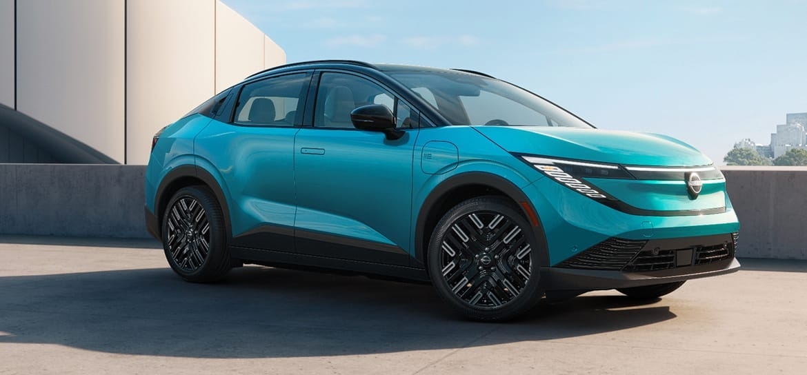 Teal 2026 Nissan LEAF parked by a modern building, viewed from the front three-quarter angle.