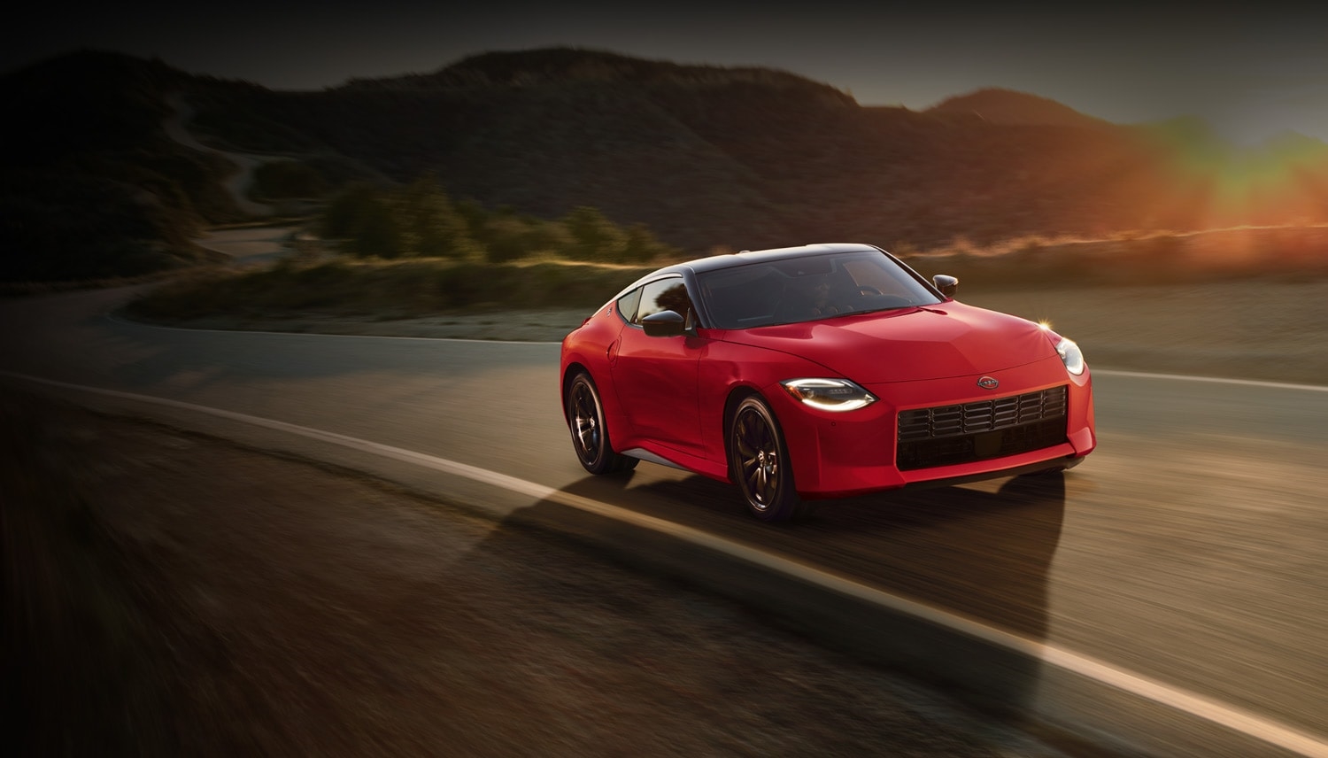 Red 2026 Nissan Z driving on a desert road at sunset, viewed from the front three-quarter angle.