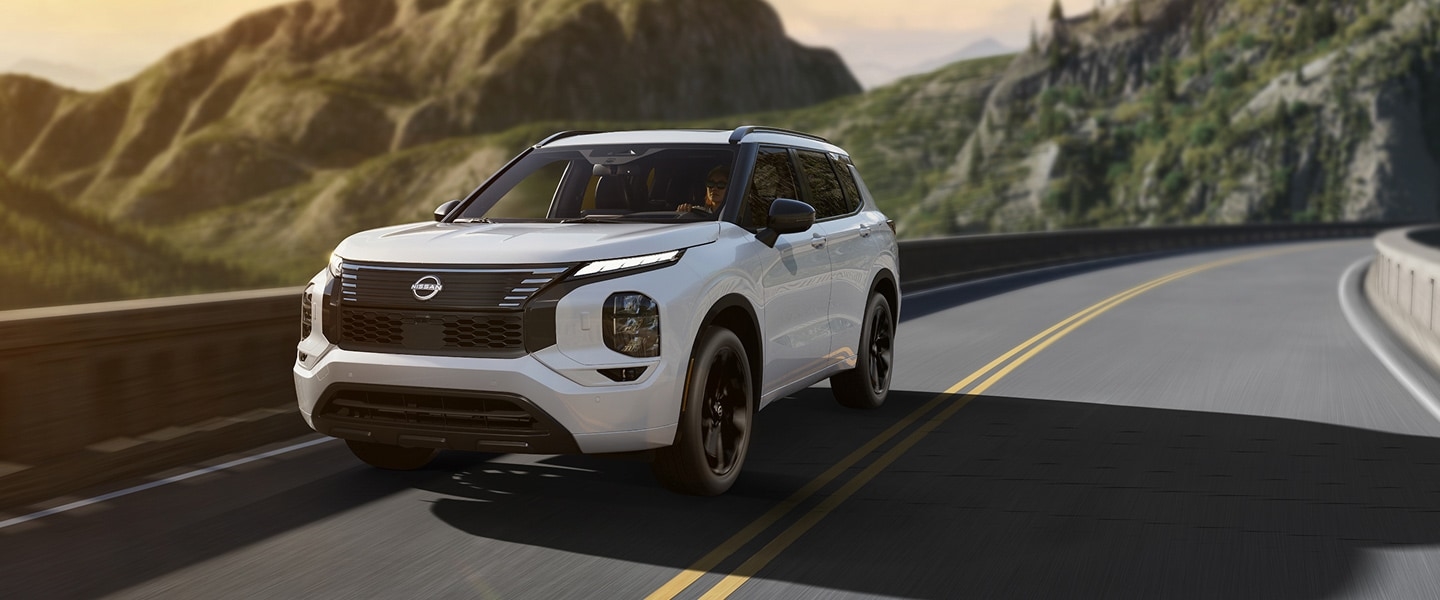 White 2026 Nissan Rogue Plug-in Hybrid driving on a mountain road, viewed from the front three-quarter angle.