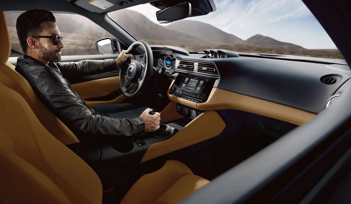 Driver at the steering wheel and manual shifter in the tan-trimmed cockpit of a 2027 Nissan Z.