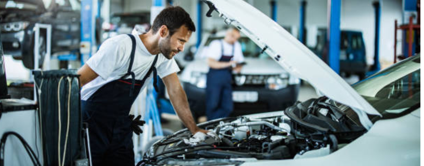 A mechanic leaning on the hood of a car looking at the internals
